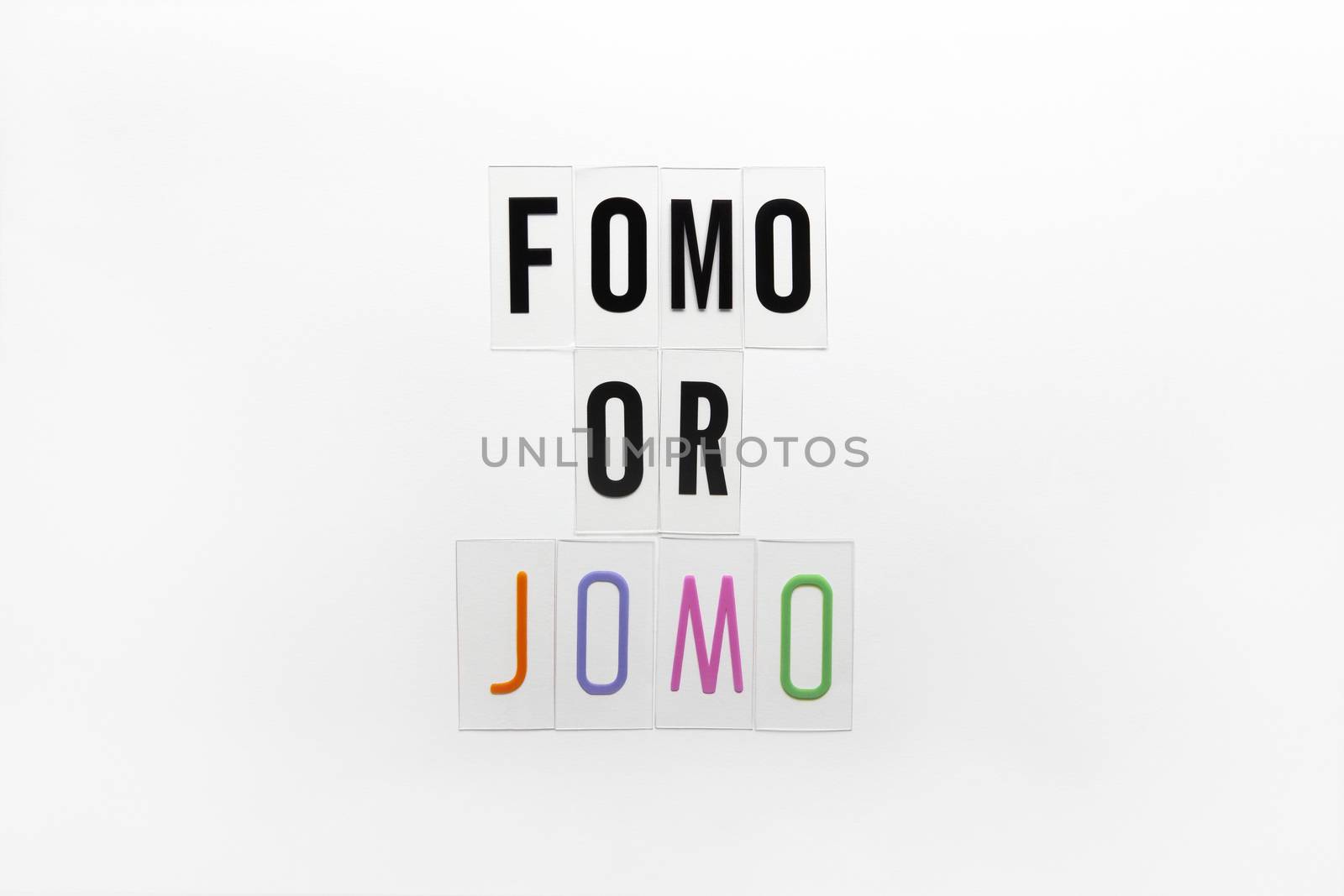 Abbreviation words FOMO, JOMO on transparent plastic on white background. FOMO means Fear Of Missing Out. JOMO - Joy Of Missing Out. Opposition, choice, social problem, digital detox. Flat lay.
