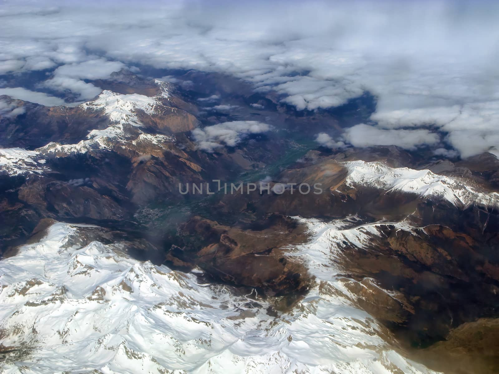 Top view of the ground from the plane. Mountain peaks of the Alps, covered with snow, among the clouds. Soft focus.