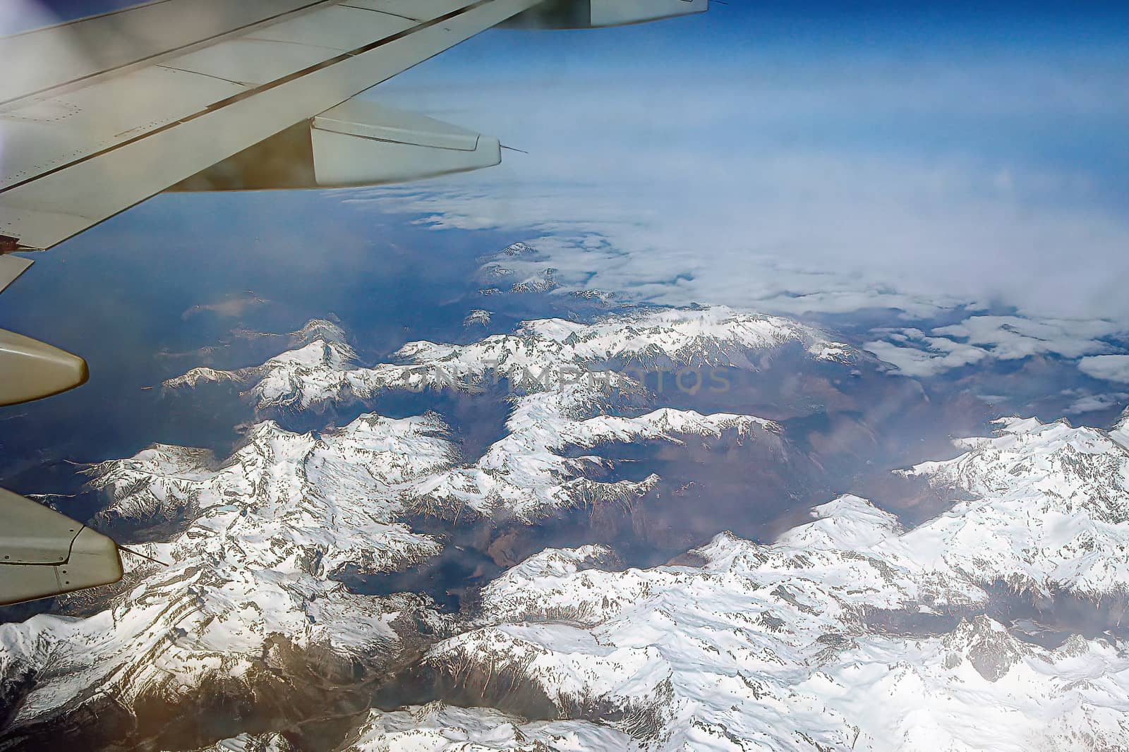 Top view of the ground from the plane. Mountain peaks of the Alps, covered with snow, among the clouds. by bonilook