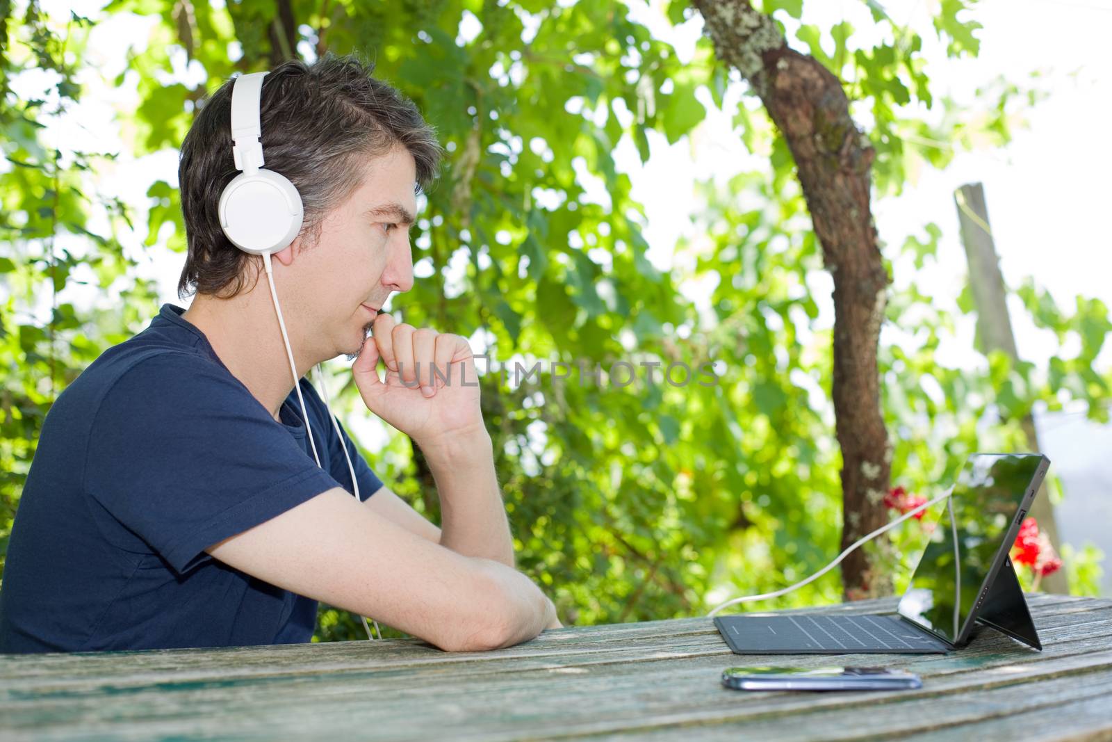 young man holding a tablet with headphones, outdoor