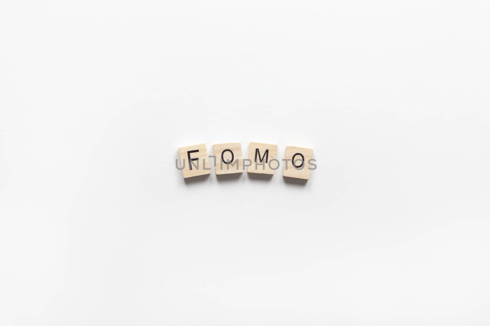 Abbreviation word FOMO from wooden blocks on white background. FOMO means Fear Of Missing Out, non-stop internet surfing. Concept social communication problem between people, digital detox. Flat lay.