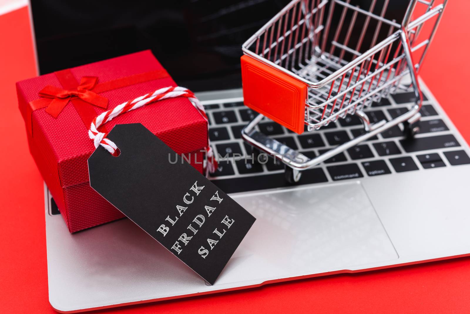 Internet online shopping marketing, top view of workspace with Black Friday text black tag, gift box and cart shopping on laptop computer on red background and have copy space for use