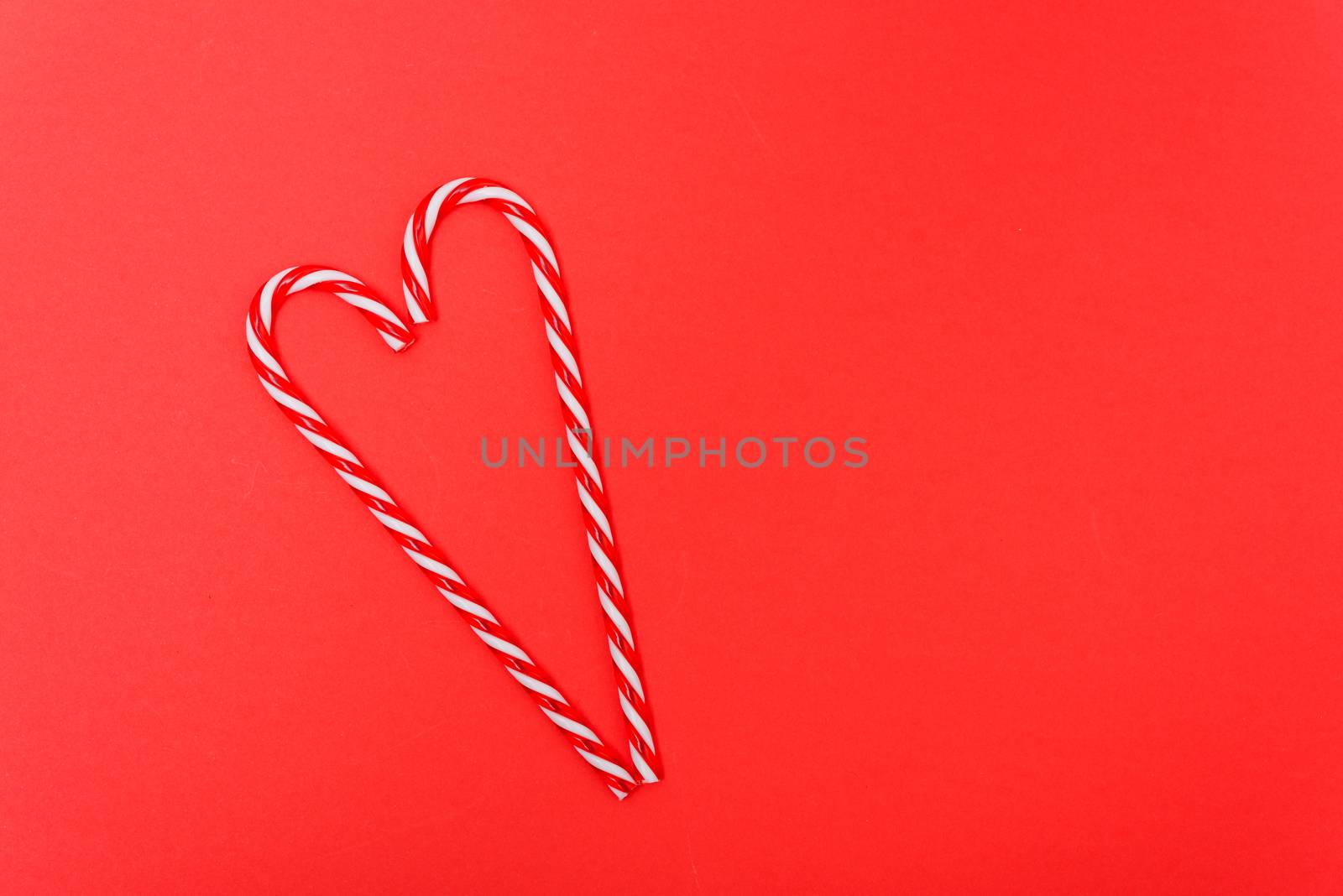 Two candy canes made making Heart of Christmas candies on red background with copy space