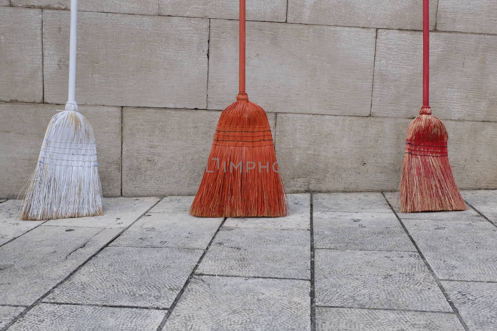 three brooms red of different colors against a wall