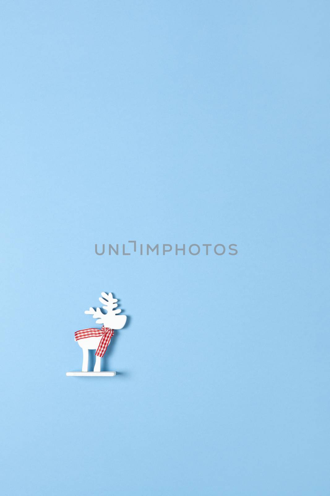 Christmas decoration, toy white deer in checkered scarf on pastel blue background with copy space. Festive, New Year concept. Vertical, flat lay. Minimal style. Top view.