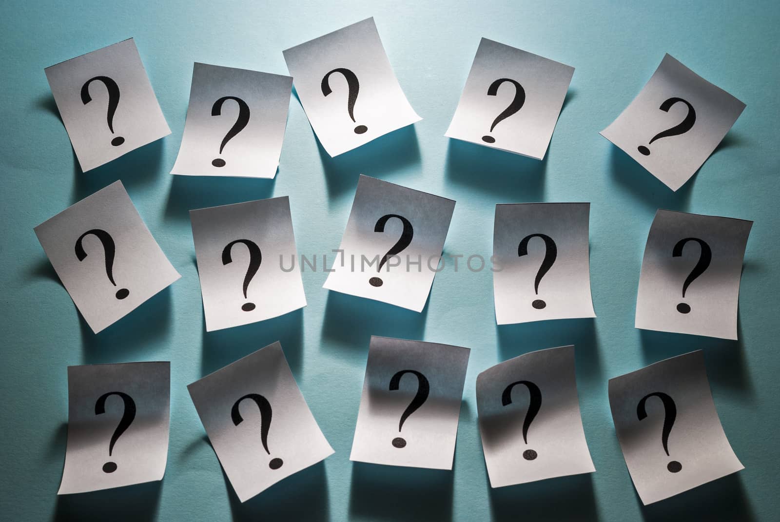Printed question marks on white cards arranged in rows on a blue background in a full frame view for a conceptual image