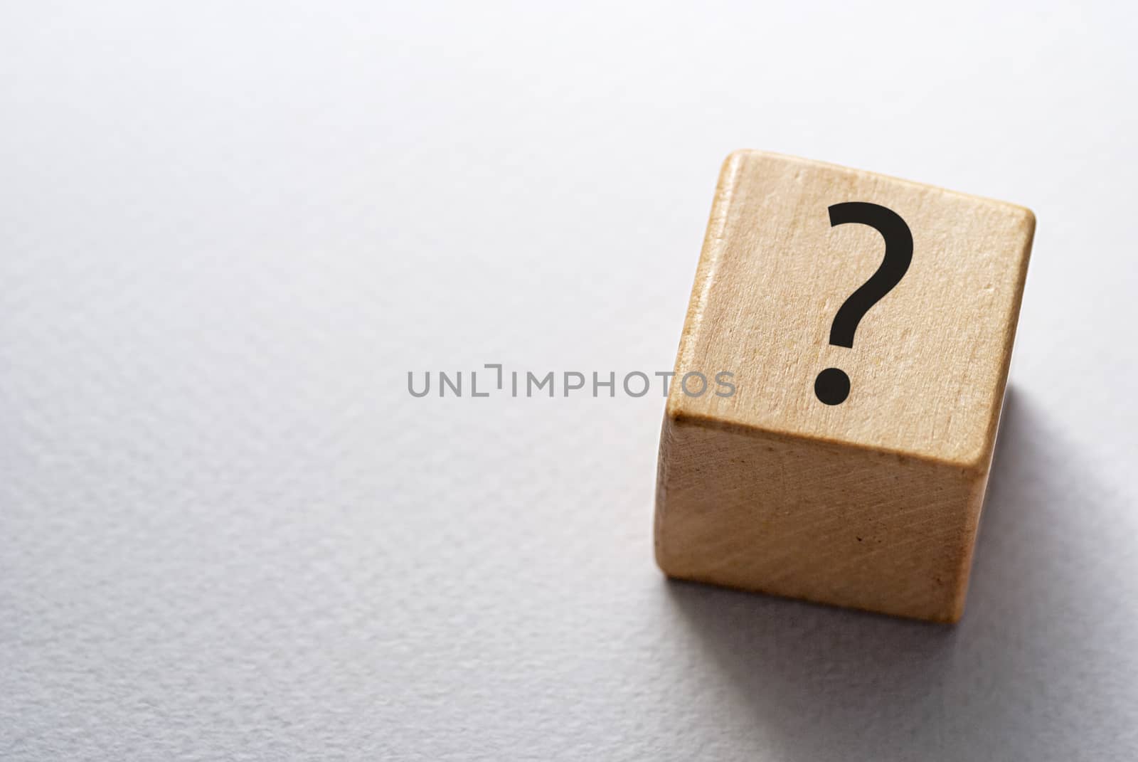 Natural wooden cube or dice with question mark viewed high angle on white with copy space