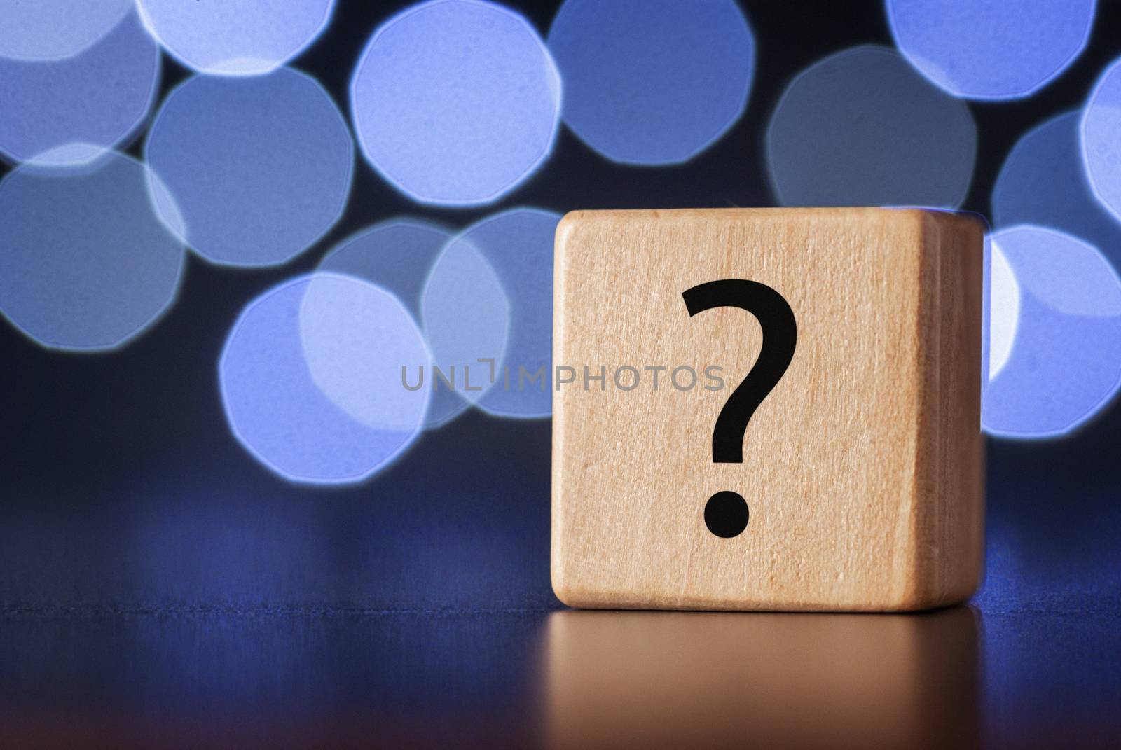 Wooden cube with question mark on a reflective table with background of white circles forming a bokeh effect