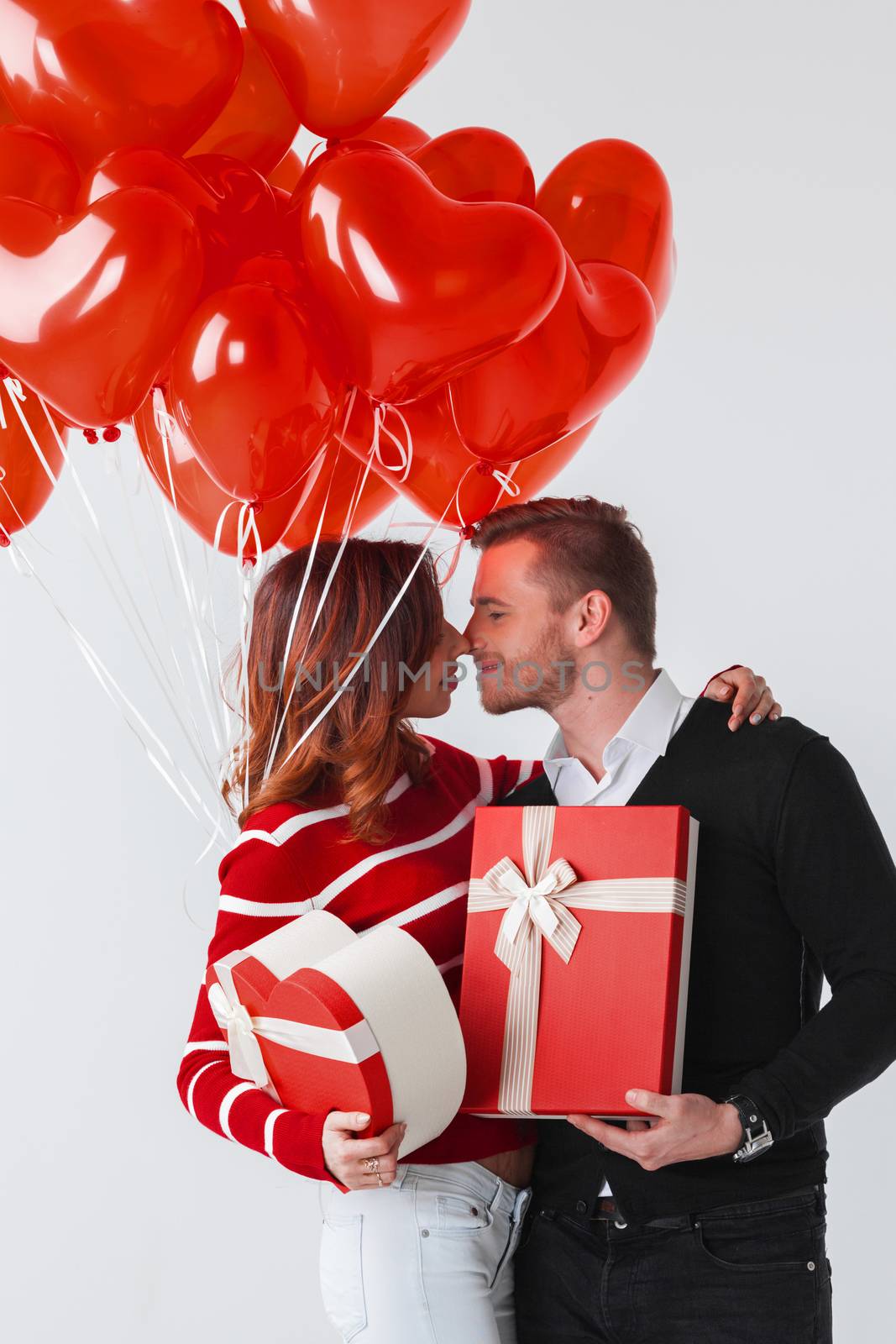 Happy smiling couple holding valentines day gifts and red balloons on white background