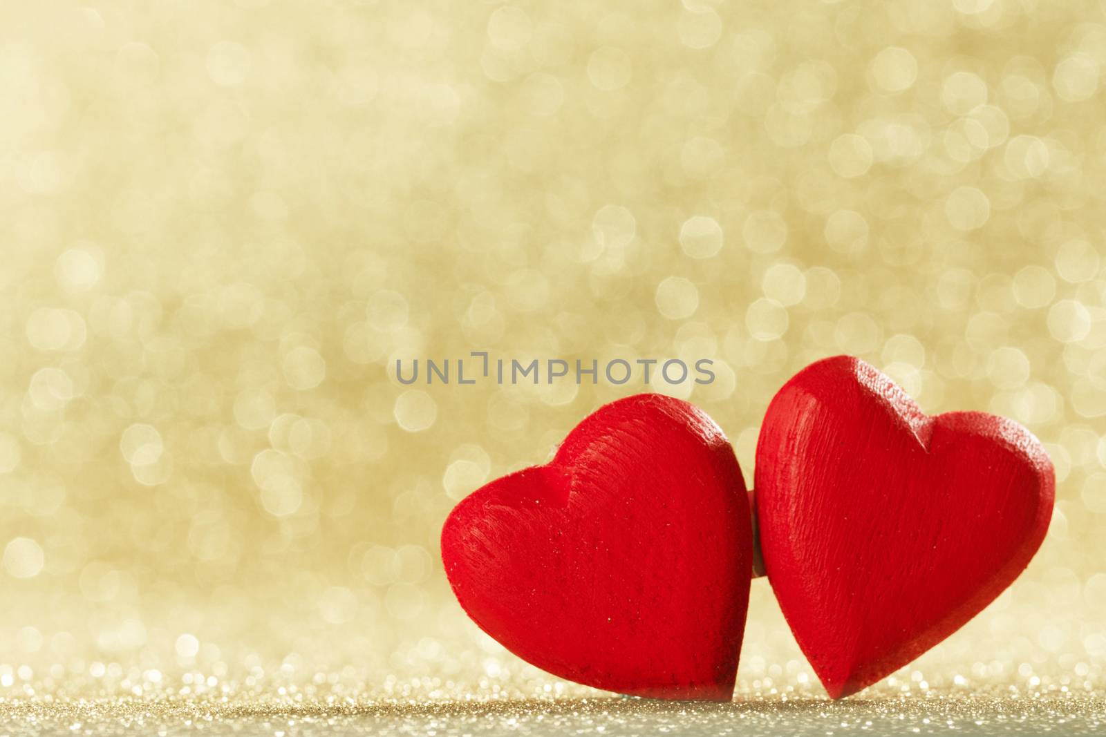Two small handmade red wooden hearts on bright golden lights bokeh background Valentines day card