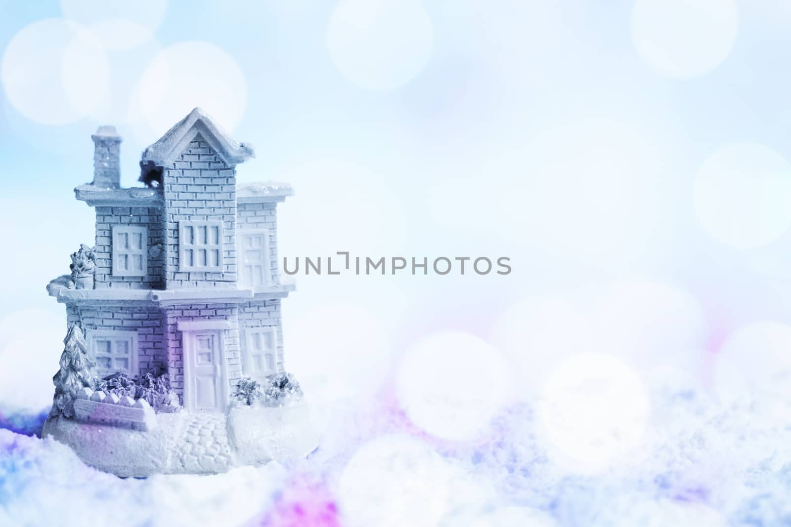 Snowy house in the snow. Winter background with colorful blue and purple shining bokeh effect. Copy space right. Shallow depth of field.