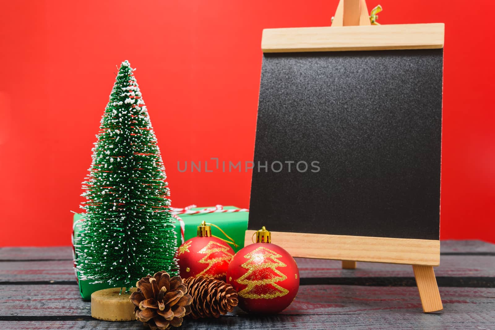 Christmas composition decorations, minimal green fir tree branches with snow and black chalkboard on red background. Merry Christmas concept. Copy space for text