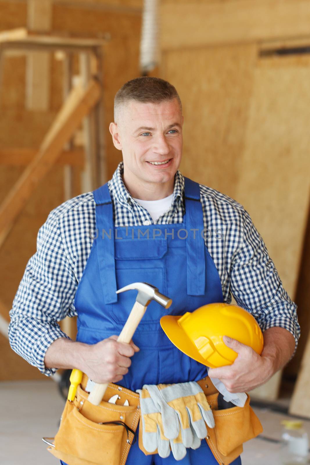 Smiling construction worker in tool belt with hammer at construction site