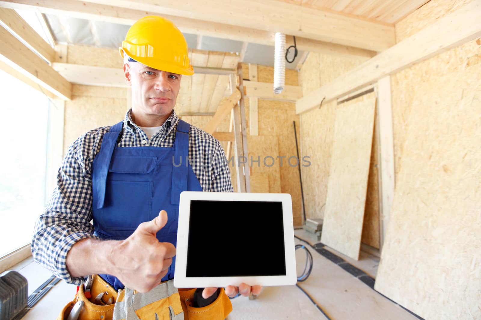 Construction worker holding digital tablet standing at construction site and showing thumb up