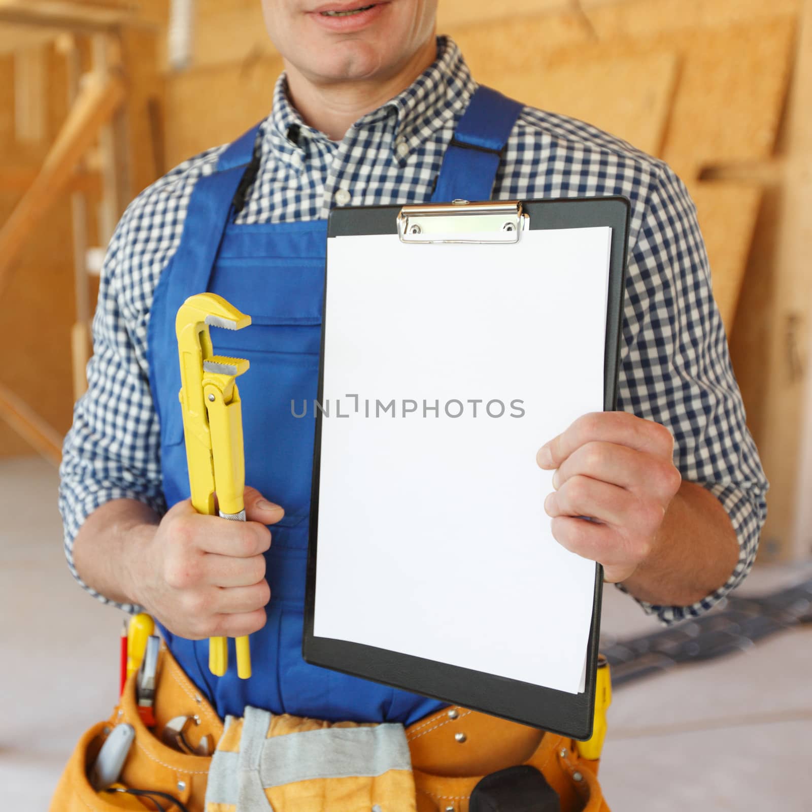 Workman with adjustable wrench and folder with blank document at construction site