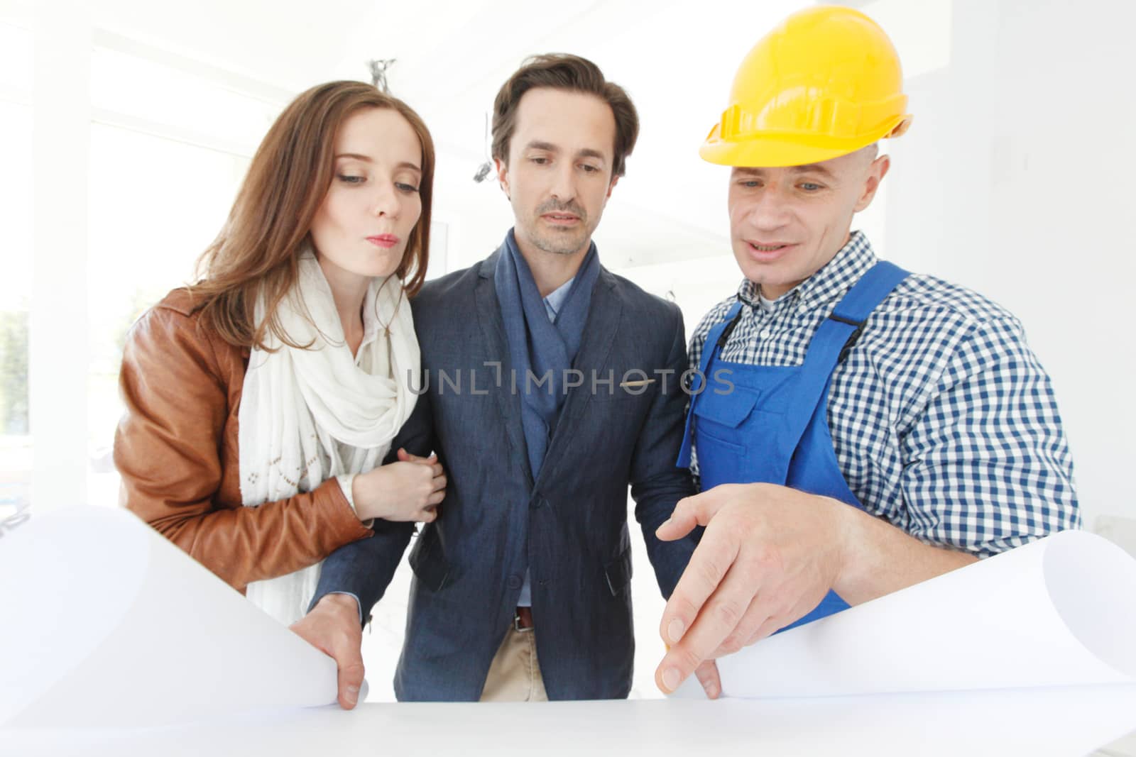 Foreman shows house design plans to a young couple at construction site