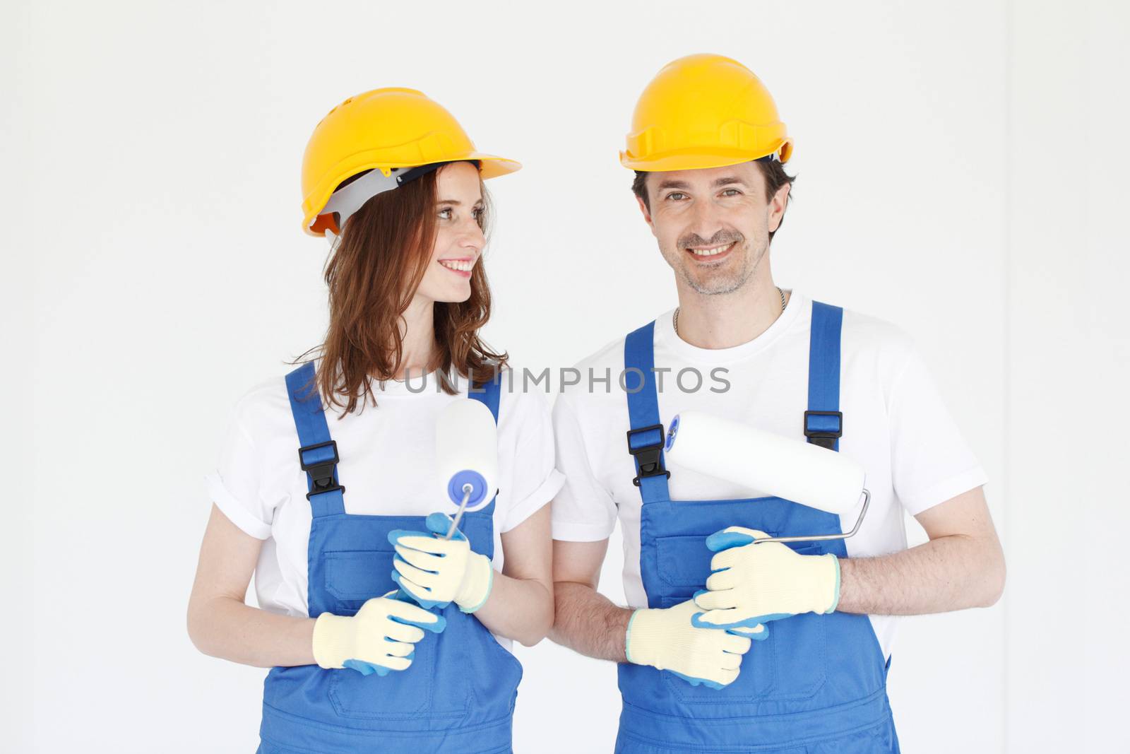 Two happy house painters in uniform holding paint rollers in new house. Repair, construction and mortgage concept.