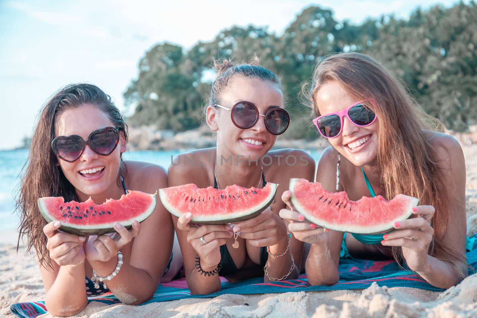Happy smiling female friends eating watermelon on beach