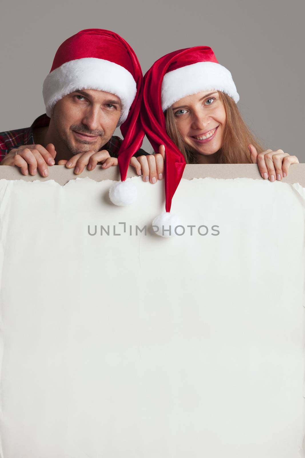 Happy couple in Santa hats holding blank banner with copy space