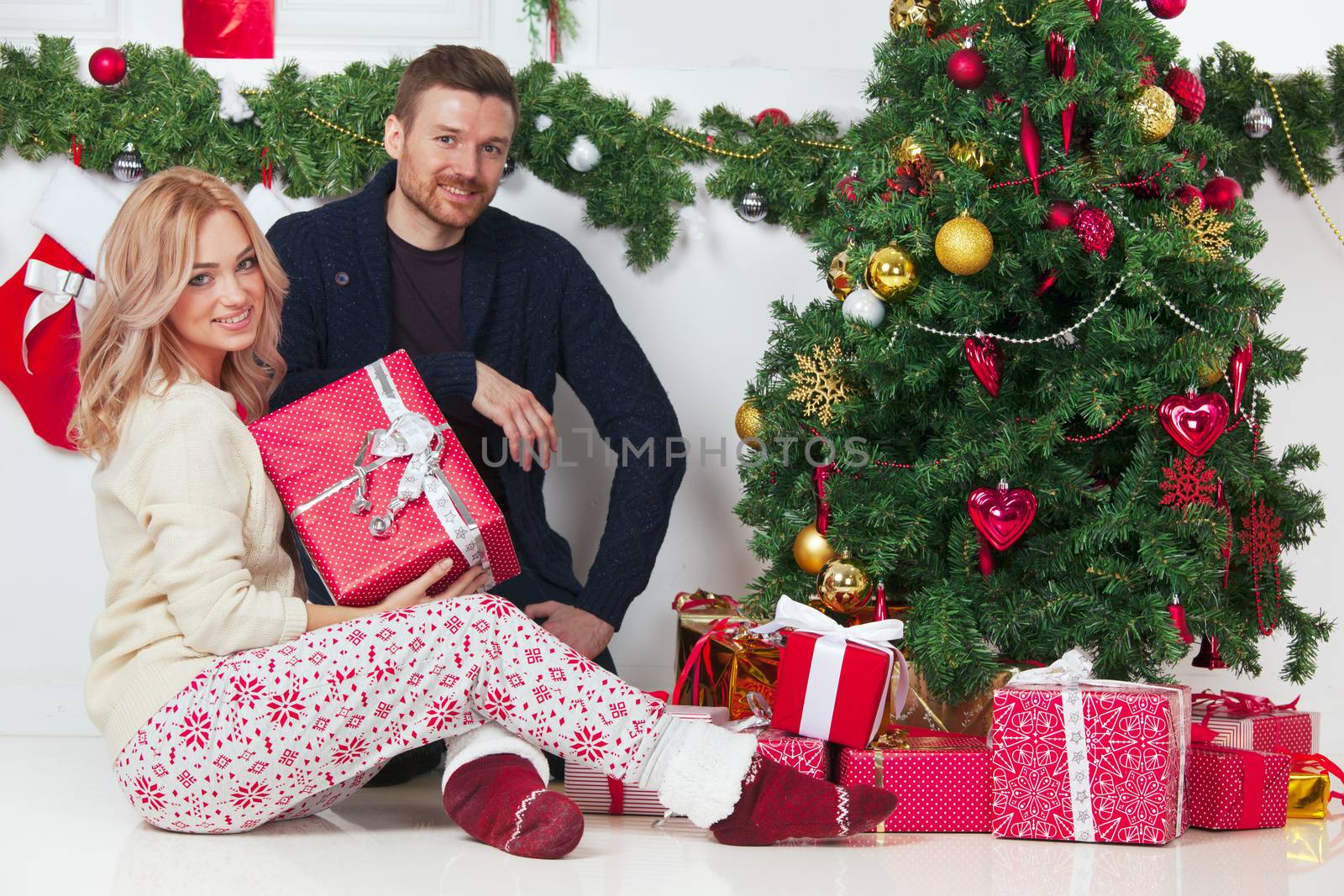 Couple in love sitting next to a nicely decorated Christmas tree, hloding Christmas gifts and smiling