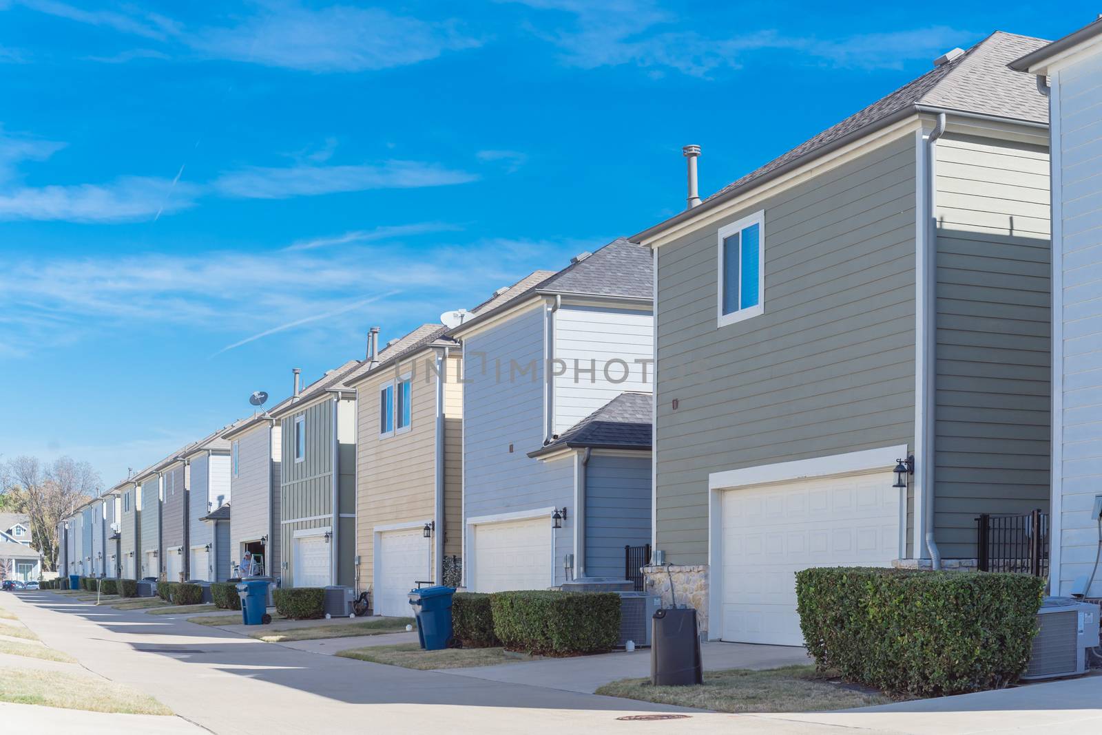 Large back alley of new development residential community, line of two-car garage door in Coppell, Texas. Colorful two story houses row well trim landscape outside of downtown Dallas, outdoor AC units