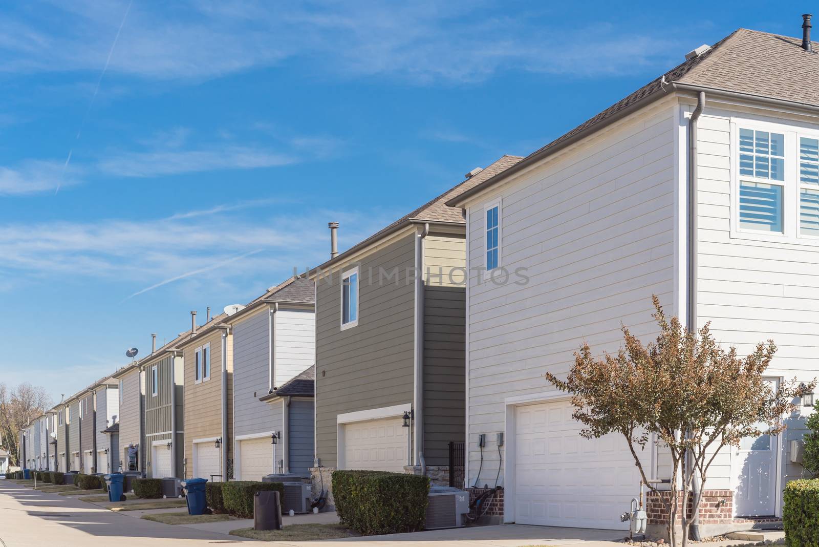 Corner house and back alley of new development residential community, line of two-car garage door in Coppell, Texas. Colorful two story houses row well trim landscape near Dallas, outdoor AC units