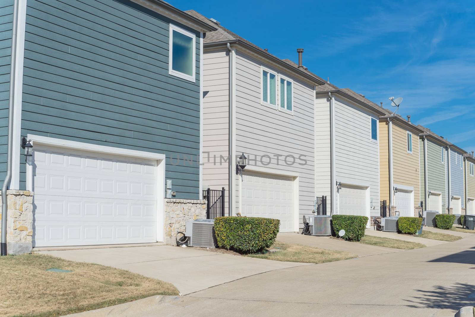 Large back alley of new development residential community, line of two-car garage door in Coppell, Texas. Colorful two story houses row well trim landscape outside of downtown Dallas, outdoor AC units