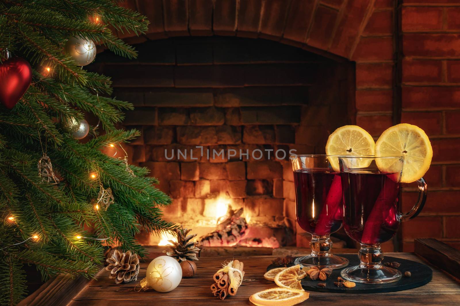 Christmas composition - two glasses with mulled wine on a wooden table near a Christmas tree opposite a burning fireplace.