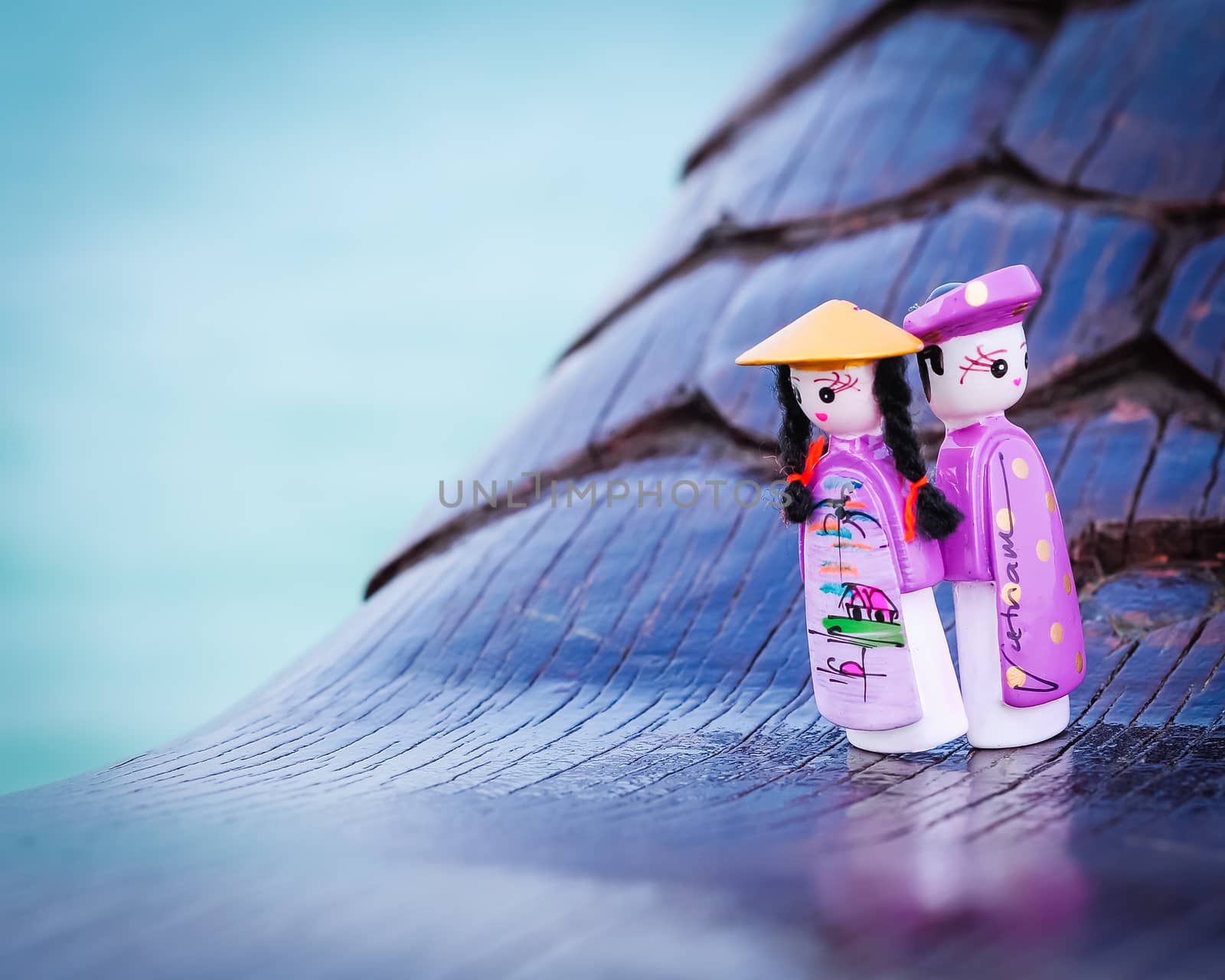 Close-up a couple handicraft magnetic wooden puppets in Vietnamese traditional costumes. Famous Vietnamese dolls souvenirs in natural set with boat and ocean background. Selective focus
