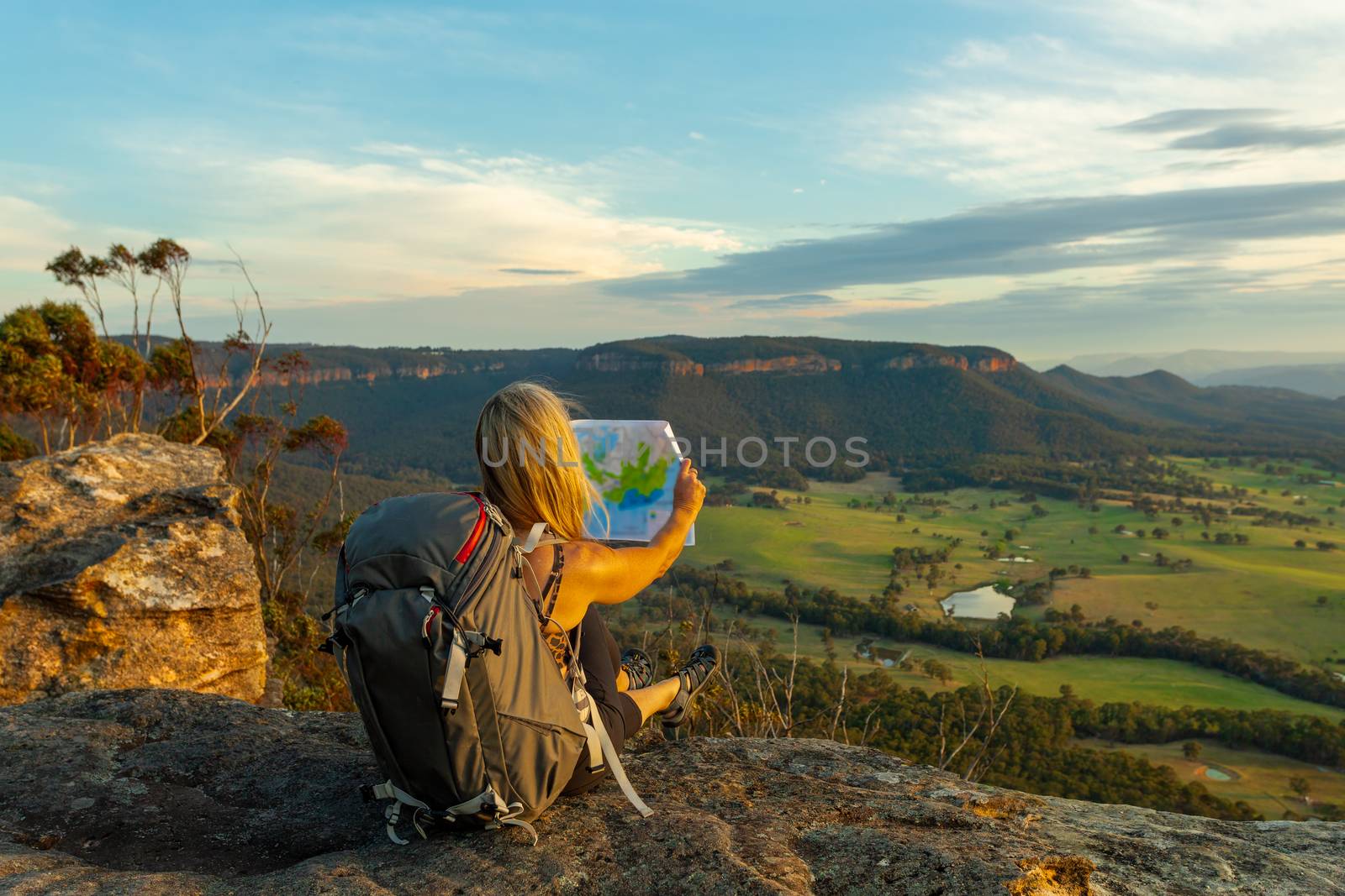 Tourist or bushwalker takes a break on a rock ledge with valley views and reads a map or other document