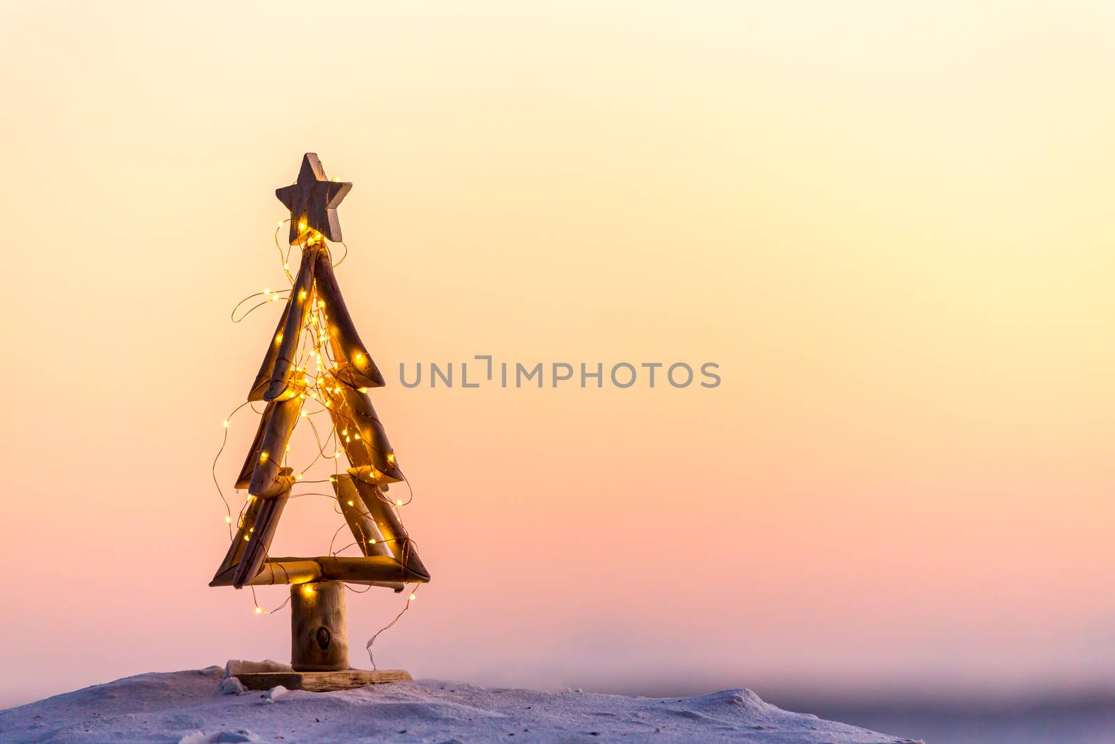 An Australian Christmas, a simple tree decorated with fairy lights on the beach in summer with warm light.  Space for message