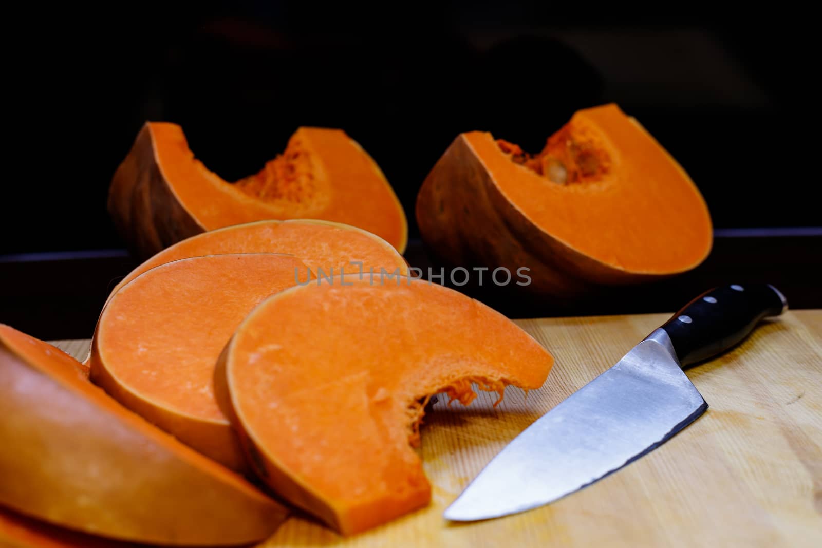 The food on thanksgiving. Pieces of bright orange pumpkin and a kitchen knife lie on a wooden Board. by bonilook