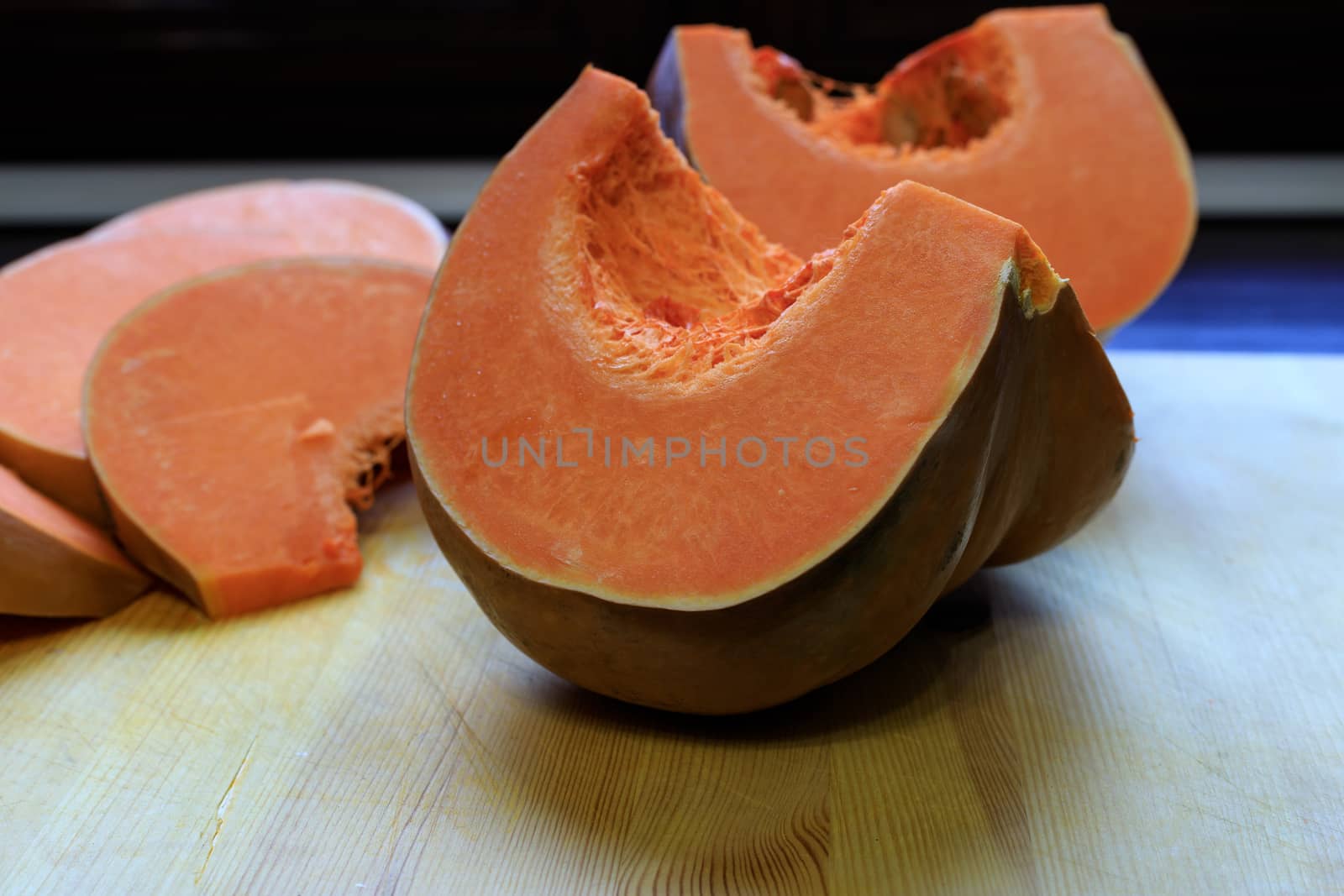 The food on thanksgiving. A bright orange pumpkin is cut into pieces with a kitchen knife and lies on a wooden Board.