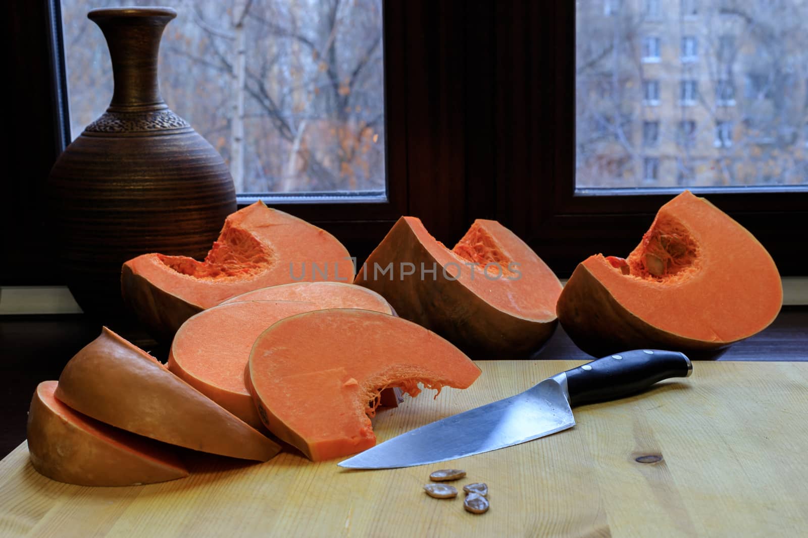 The food on thanksgiving. A bright orange pumpkin is cut into pieces with a kitchen knife and lies on a wooden Board.