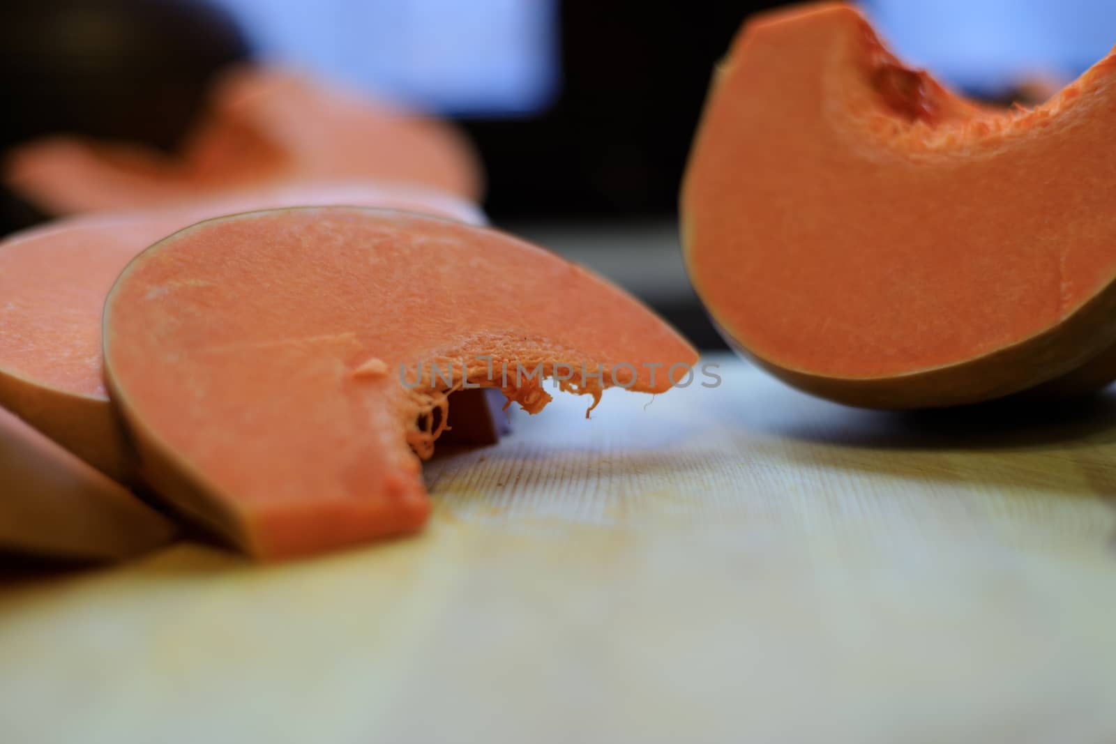 The food on thanksgiving. A bright orange pumpkin is cut into pieces with a kitchen knife and lies on a wooden Board.