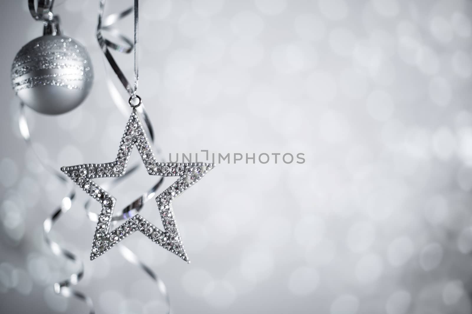 Silver Christmas new year balls and star with curly streamer ribbon bow over glittering bokeh lights background with copy space for text