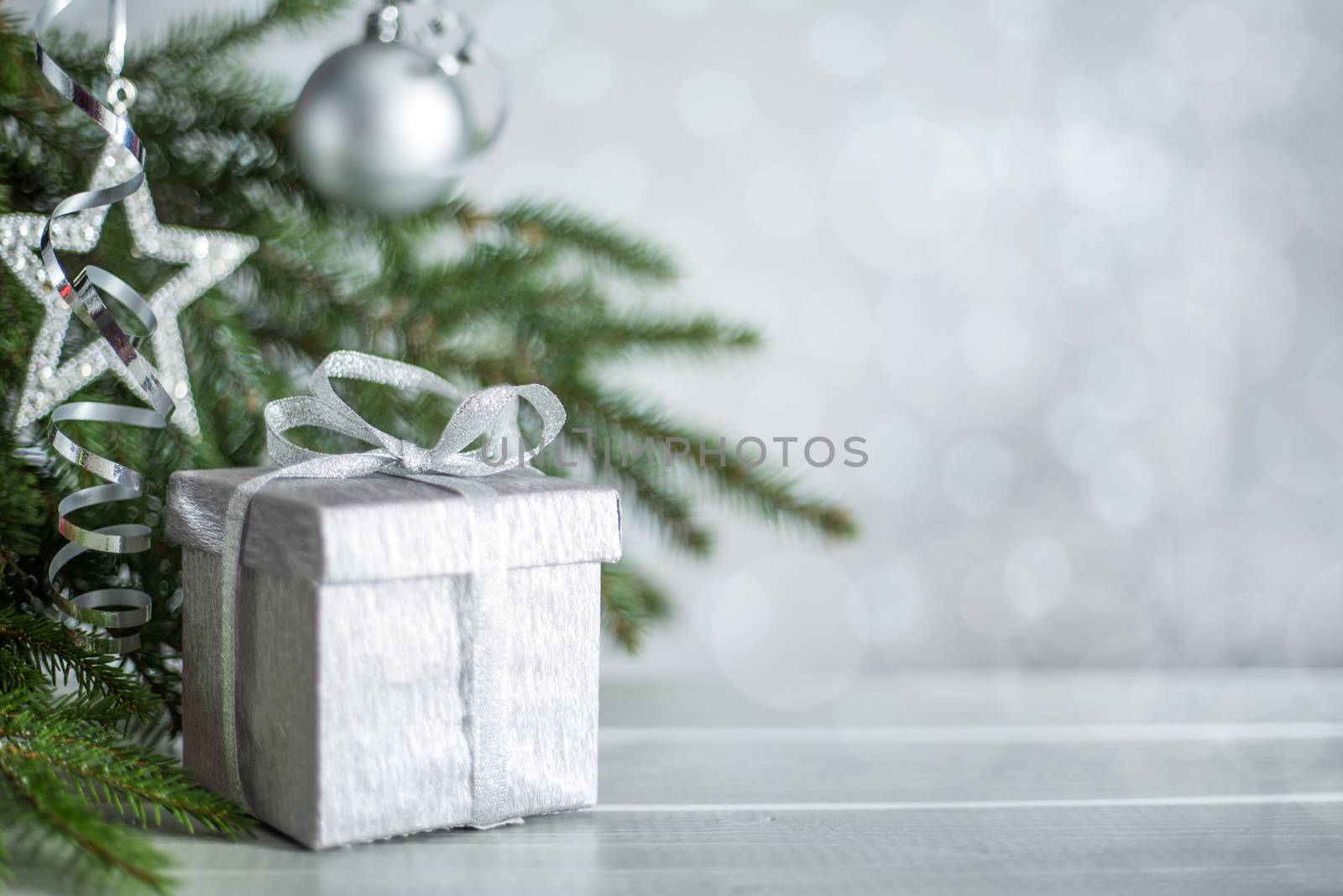 Silver Christmas new year gift with curly streamer ribbon bow over glittering bokeh lights background under fir tree with baubles