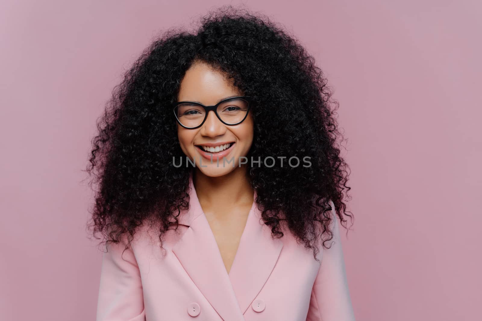 Close up portrait of happy curly haired woman has gentle smile on face, dark healthy skin bushy hair, wears elegant clothes, isolated on purple background, enjoys coming weekend, works in office by vkstock