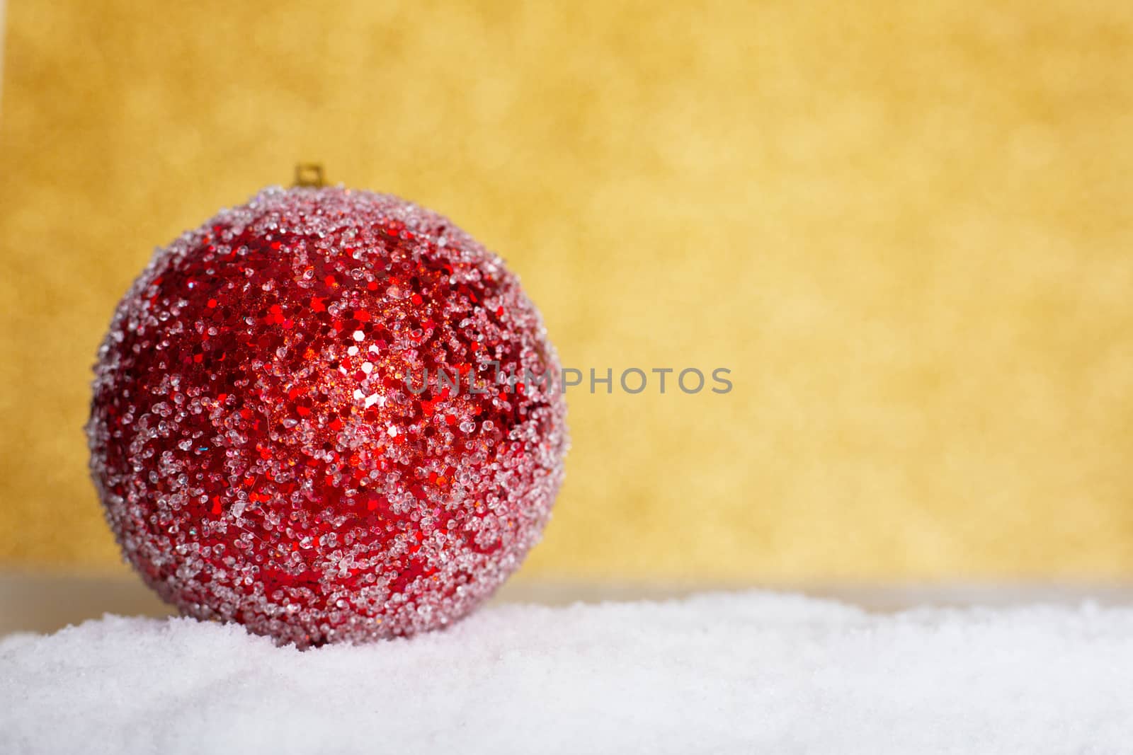 Christmas red ball on snow over golden glitter background with copy space for text
