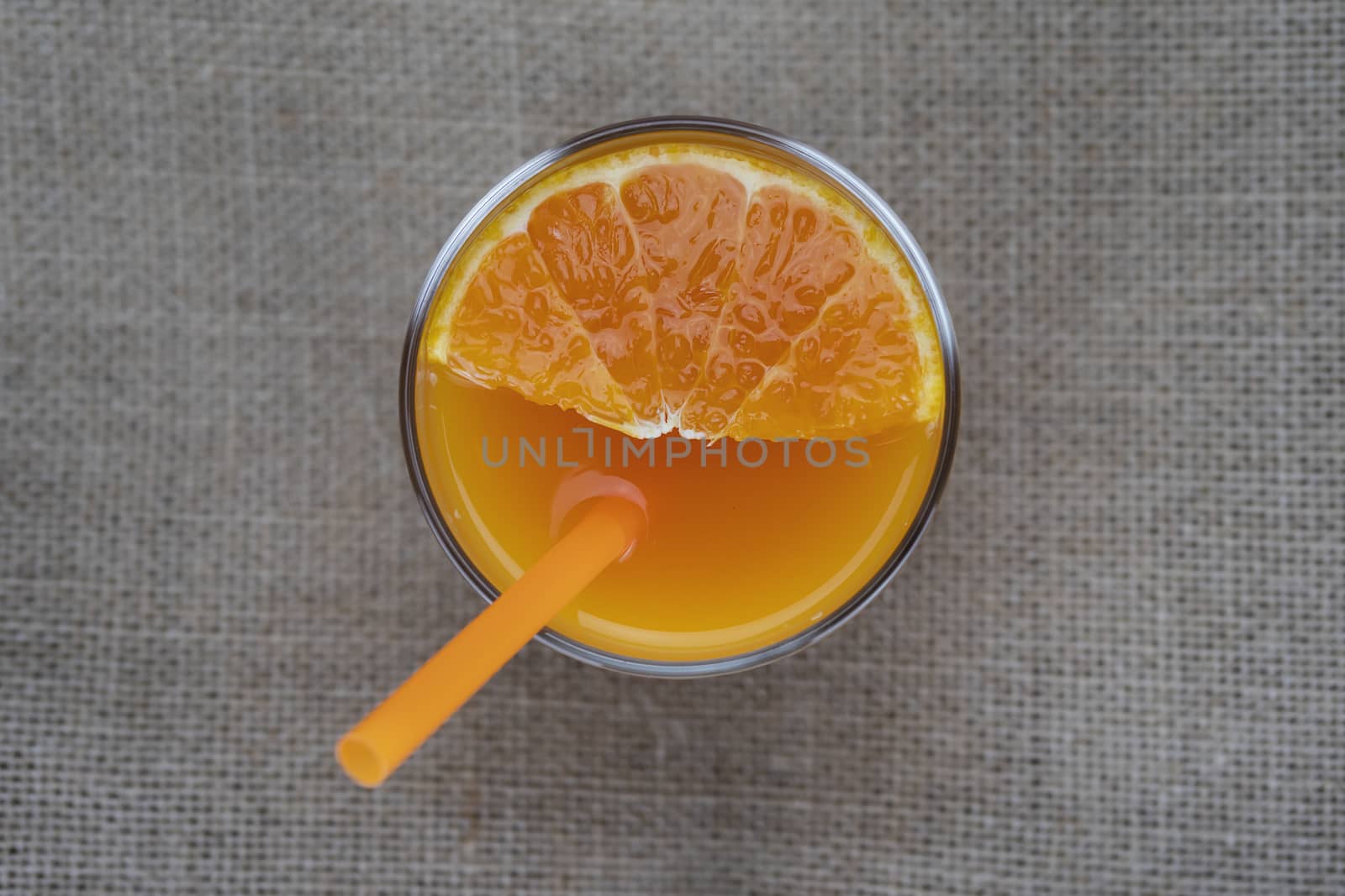 Fresh orange juice glass with orange straw over sack fabric background - tropical orange fruit juicy drink for background use