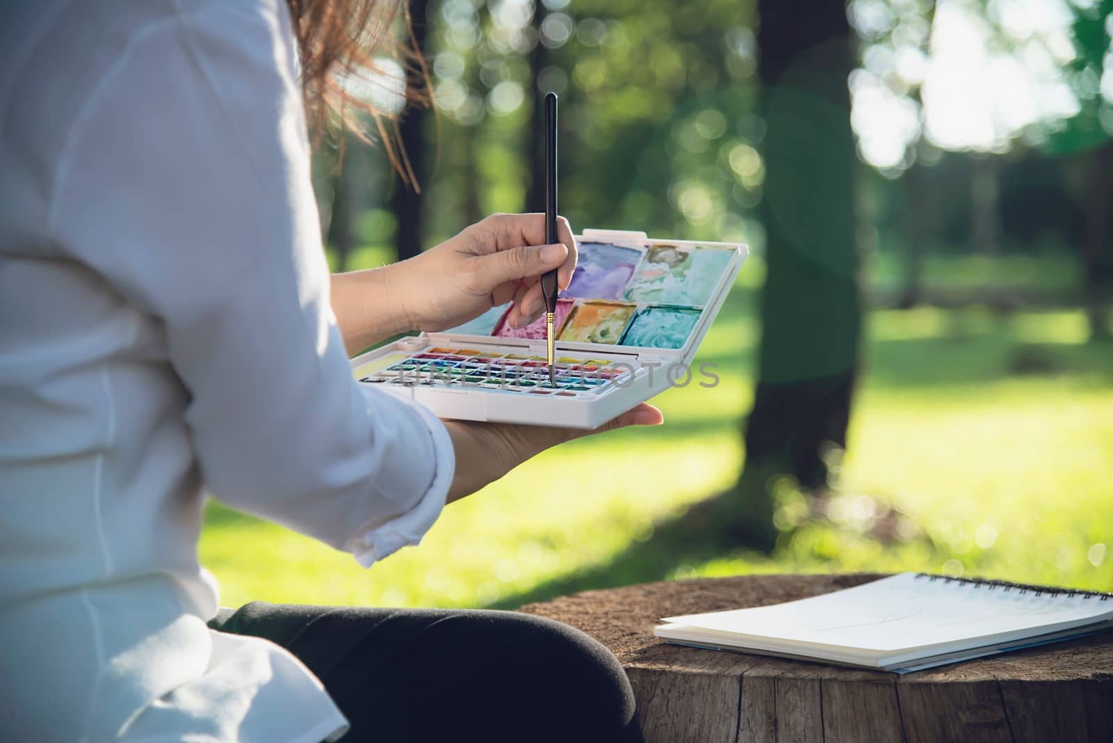 Relax woman painting water colour art work in green garden forest nature - people with creative art in nature stress reduction and meditation concept