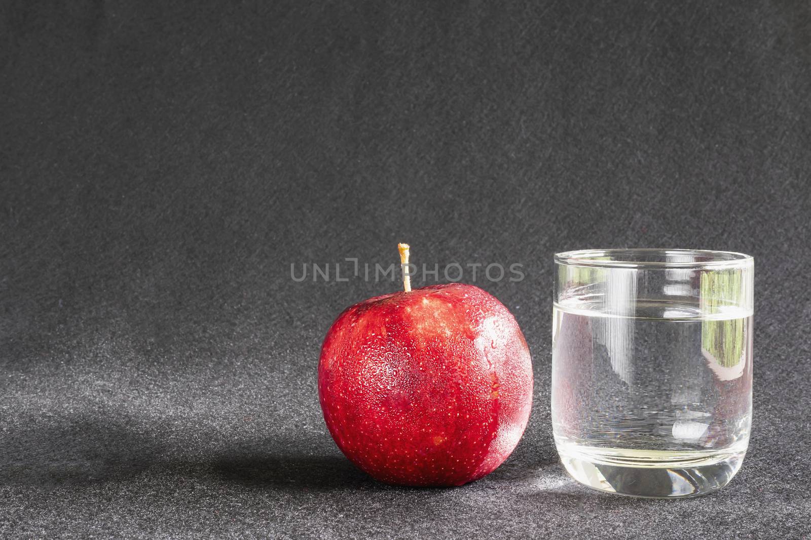 Fresh apple with glass of clean drinking water over gray background - clean fresh fruit and water background concept