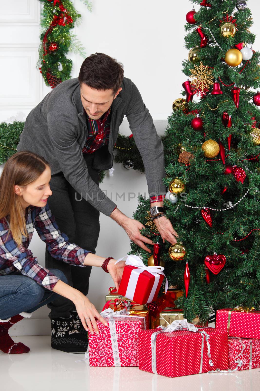 Couple in love sitting next to a nicely decorated Christmas tree, holding Christmas gifts and smiling