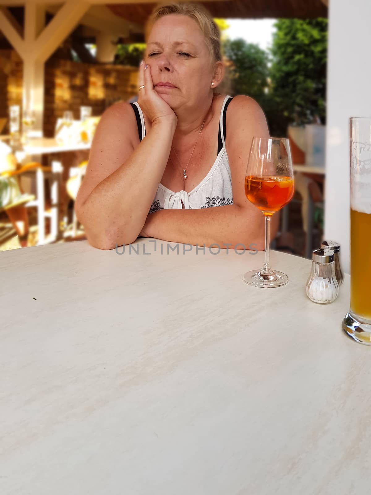 Close-up a woman at sits in a restaurant at the table in the foreground a glass of beer with blurred background.