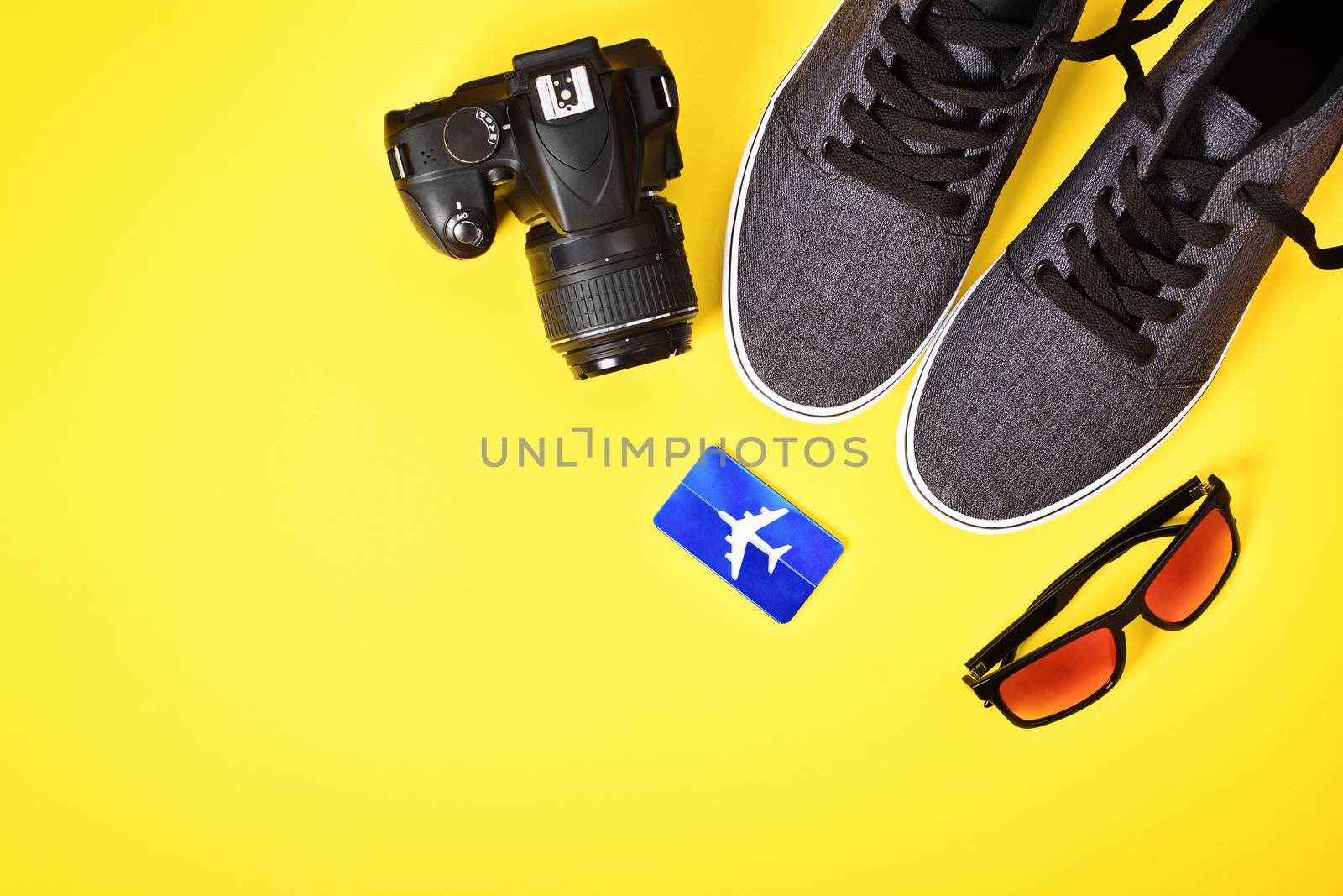 Vacation concept. Top view of camera, airplane luggage tag, sunglasses and sneakers on a yellow background. These are my travel essentials for a trip around the world or just a weekend getaway. Flat lay, copy space.