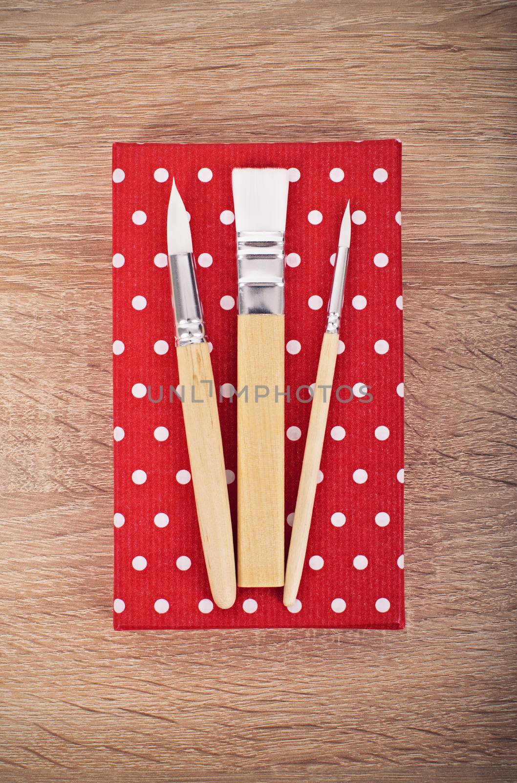 Painting concept. Paintbrushes in different size laid out on a red polka dot box placed on a wooden table.