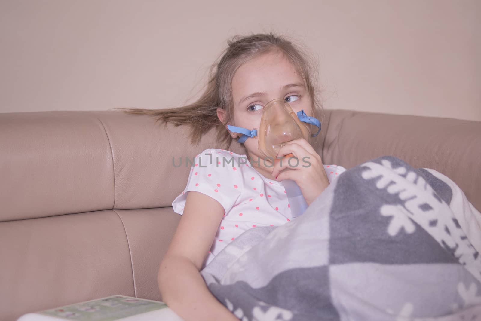 The little girl does inhalation at home.The girl sits with inhalation. The child is sick and sad. The little girl feels bad.