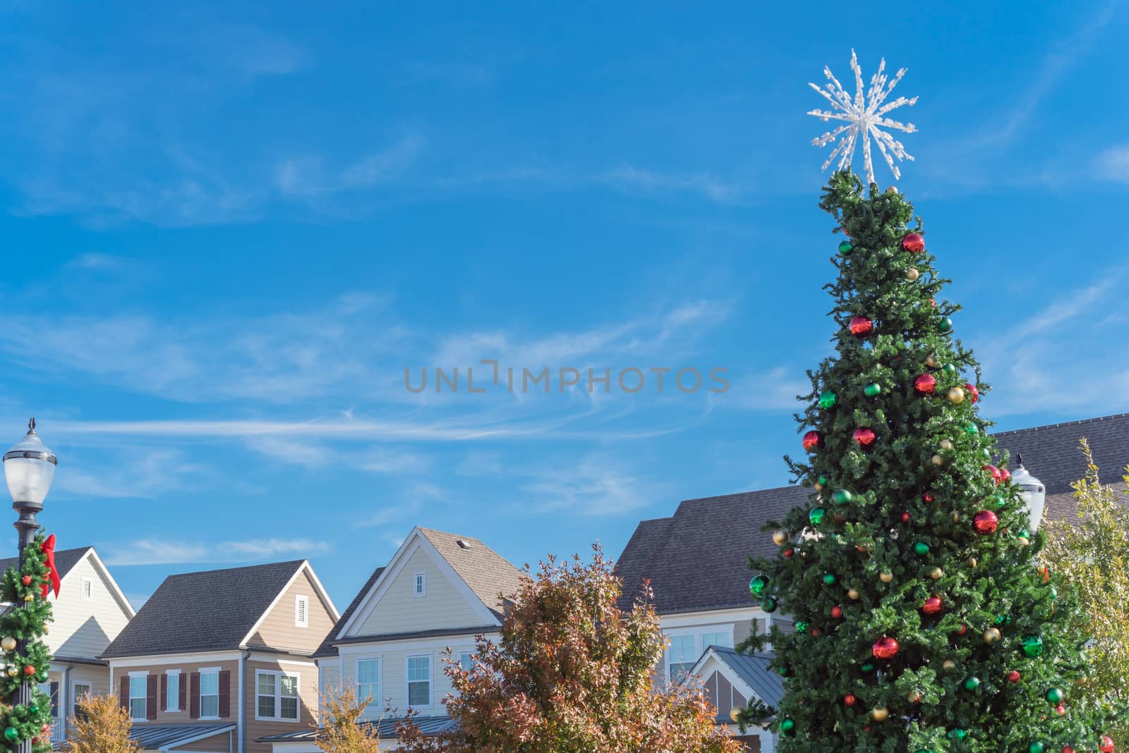 Huge Christmas tree with snowflake tree topper and colorful glass ornaments balls on display at City Square in Coppell, Texas, USA. Christmas decoration row of country-style houses near Dallas