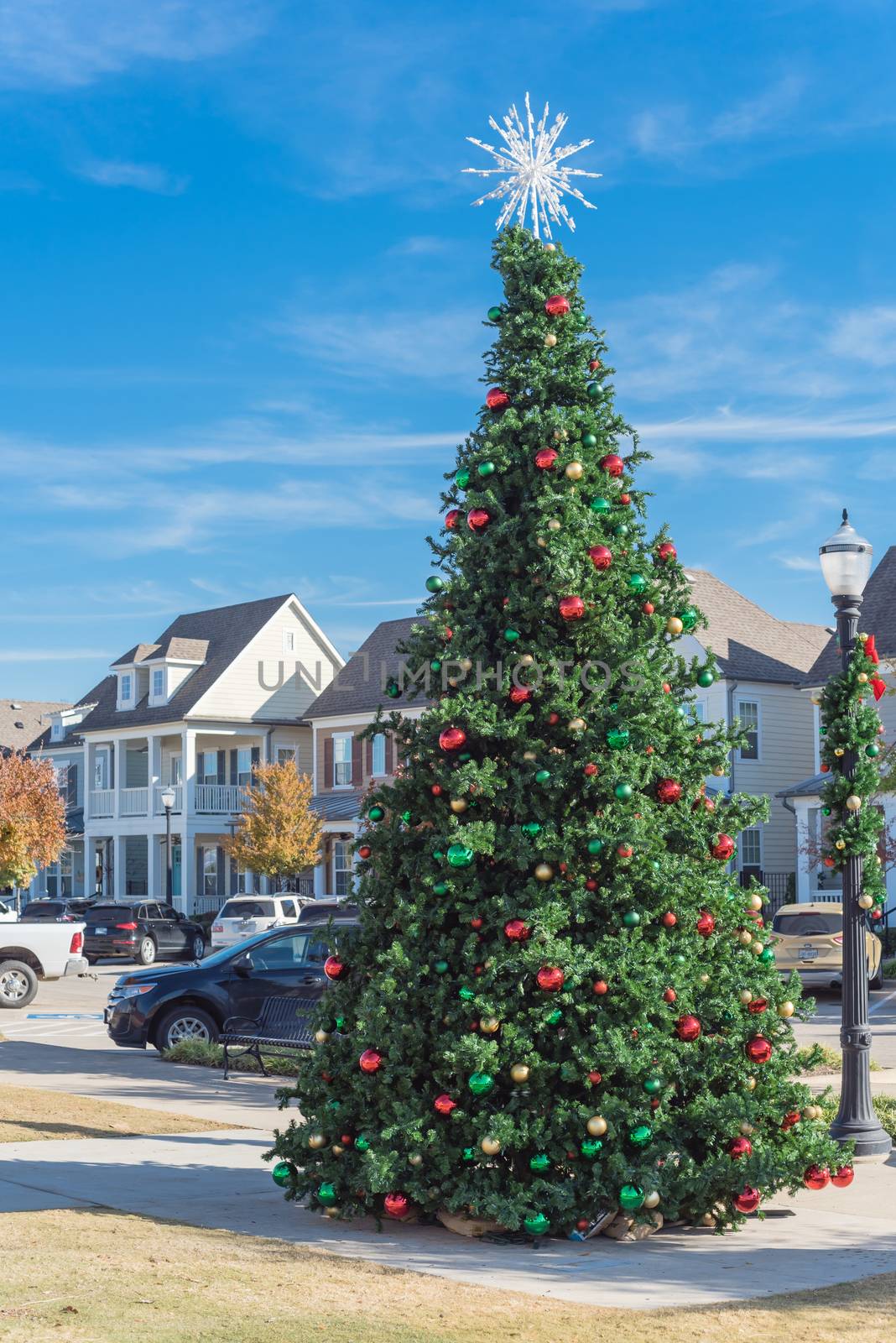 Giant Christmas tree with snowflake tree topper and colorful glass ornaments ball on display at City Square park in Coppell, Texas, USA. Xmas decoration with parked cars and country-style houses