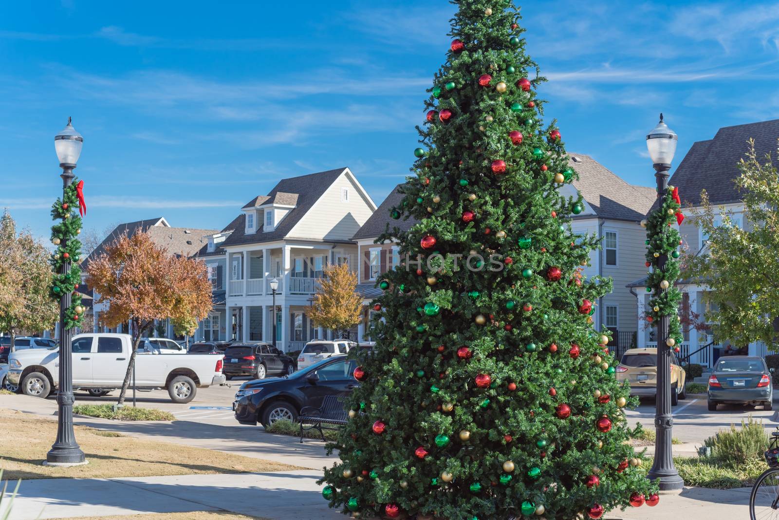 Giant Christmas tree with snowflake tree topper and colorful glass ornaments ball on display at City Square park in Coppell, Texas, USA. Xmas decoration with parked cars and country-style houses